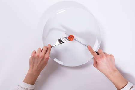 A Person's Hand Cutting Cherry Tomato On Plate With Knife And Fork