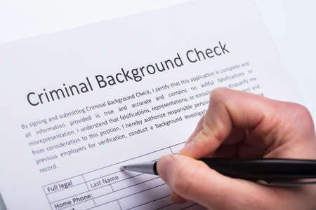 Close-up Of A Person's Hand Filling Criminal Background Check Form With Penの写真素材