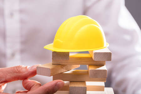 Yellow Hardhat Over Businessperson's Hand Stacking Wooden Blocksの写真素材