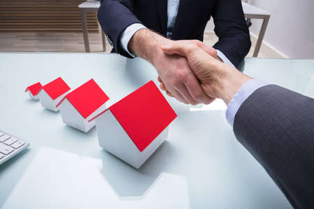 Two Business Partners Shaking Hand Near Various Size Of House Models On Deskの写真素材