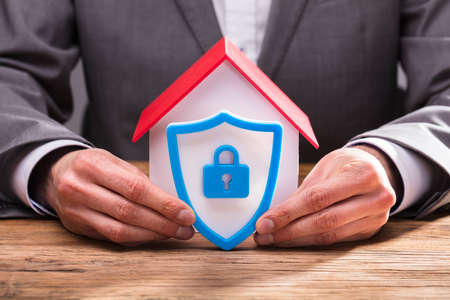 Close-up Of A Businessperson's Hand Holding Shield Security Icon Besides House Modelの写真素材