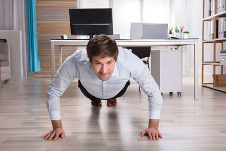 Side View Of A Young Businessman Doing Push Up In Officeの写真素材