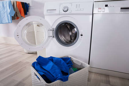 Empty Washing Machine With Pile Of Dirty Clothes In Basket At Laundry Room
