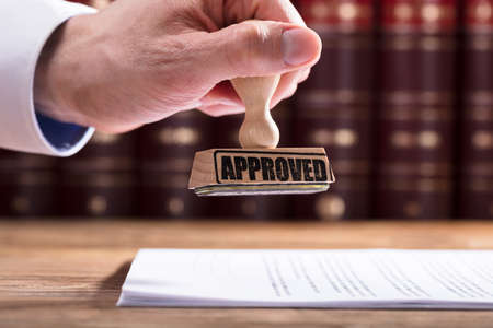 Close-up Of A Judge's Hand Approving Contract Form In Courtroomの写真素材