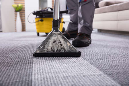 Low Section Of A Person Cleaning The Carpet With Vacuum Cleaner In Living Roomの写真素材