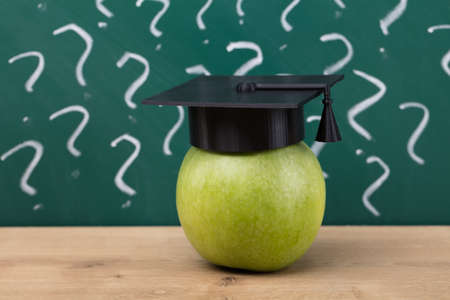 Green Apple With Graduation Hat In Front Of Chalkboard Showing Question Mark Signs