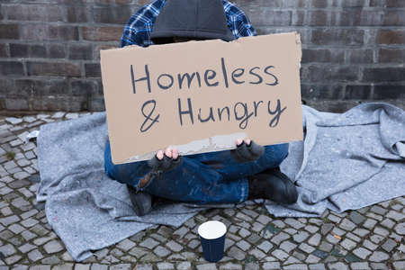 Male Beggar Lying On Street With Homeless And Hungry Text On Cardboardの写真素材
