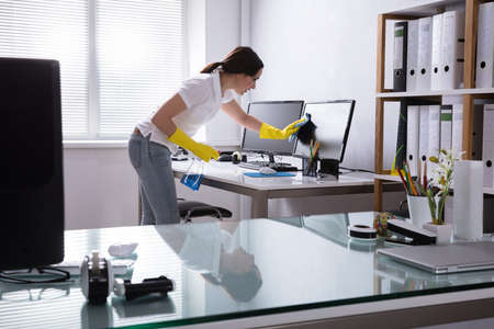 Young Woman Cleaning Computer With Rag In Officeの写真素材