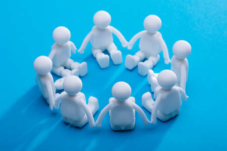 Close-up Of Human Figures Forming Circle Sitting On Blue Backgroundの写真素材