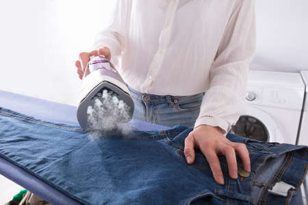 Close-up Of A Woman's Hand Ironing Jeans With Electric Ironの写真素材