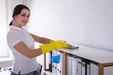Side View Of A Happy Female Janitor Cleaning Shelf With Rag