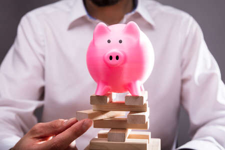 Close-up Of Piggybank Over Businessperson's Hand Arranging Wooden Blocks