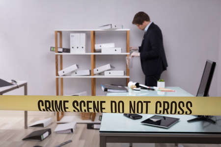 Investigator Collecting Evidence In Office Behind Yellow Crime Scene Tape