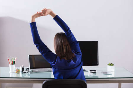 Close-up Of A Young Businesswoman Stretching Her Arms At Workplaceの写真素材