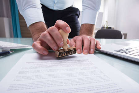 Close-up Of A Businessman's Hand Stamping Approved On Document In Office