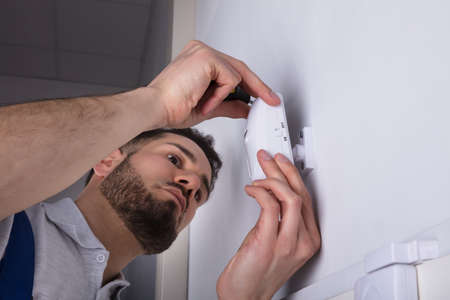 Close-up Of A Young Male Electrician Installing Security System Door Sensor On Wallの写真素材