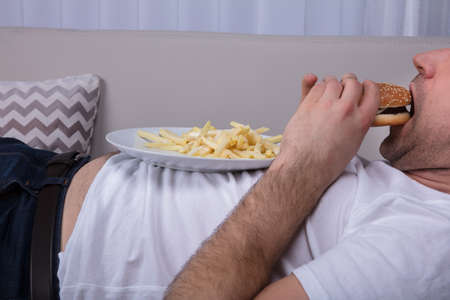 Close-up Of A Man Eating Burger And French Fries On Plateの写真素材