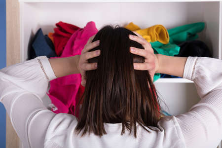 Rear View Of A Young Woman With Hand On Head In Front Of Cloth Shelf