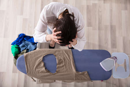 Elevated View Of A Sad Woman Standing By Ironing Board With Burned Clothの写真素材