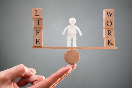 A Person's Hand With Human Figure Standing Between Work And Life Wooden Blocks On Seesawの写真素材