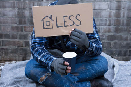 Beggar's Hand Wearing Gloves Holding Homeless Placard In Front Of His Face