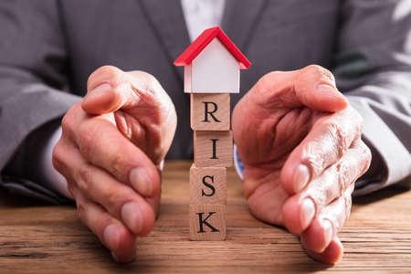 Businessperson's Hand Protecting Risk Wooden Blocks With House Modelの写真素材