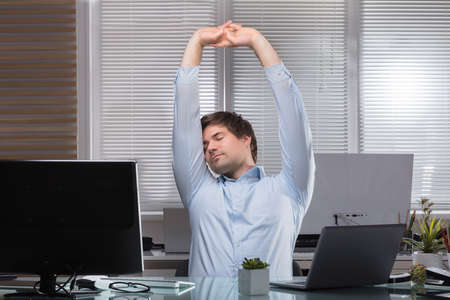 Tired Young Businessman Stretching His Arms At Workplaceの写真素材