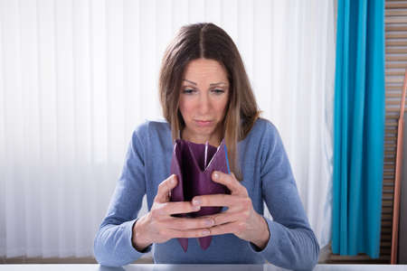 Close-up Of Unhappy Mature Woman Showing Her Empty Purse On Desk In Office