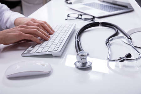 Doctor's Hand Using Computer Keyboard With Stethoscope On Deskの写真素材