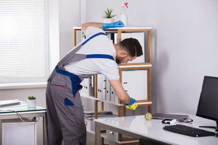 Close-up Of A Young Male Cleaner Cleaning Shelf At Workplaceの写真素材