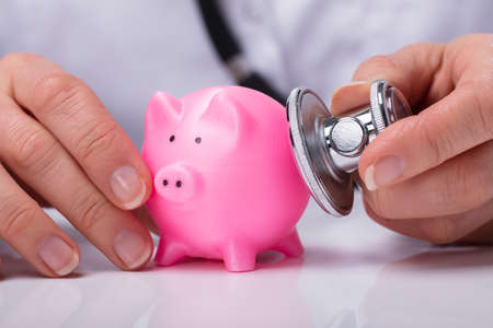 Doctor's Hand Examining Pink Piggybank With Stethoscopeの写真素材