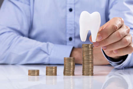 Man Placing Coin On Top Of The Stack Coins In Front Of White Tooth