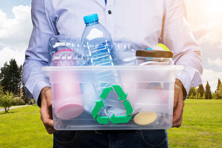 Person's Hand Carrying Recycle Container Full Of Plastic Bottles