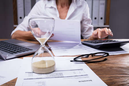 Close-up Of A Hourglass On Invoice In Front Of Businesswoman Working On Documentの写真素材
