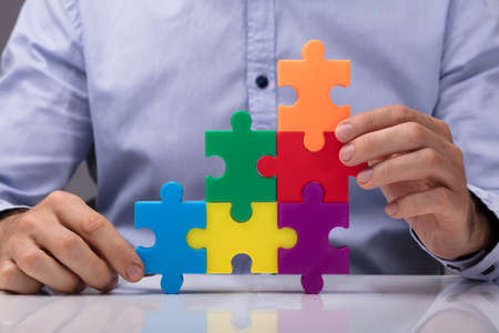 A Person's Hand Building Staircase With Multicolored Jigsaw Puzzle