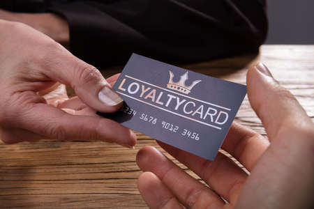 Human Hand Giving Loyalty Card To Another Person Over Wooden Deskの写真素材