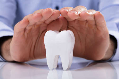 Man's Hand Protecting Healthy Hygienic White Tooth On Reflective Tableの写真素材