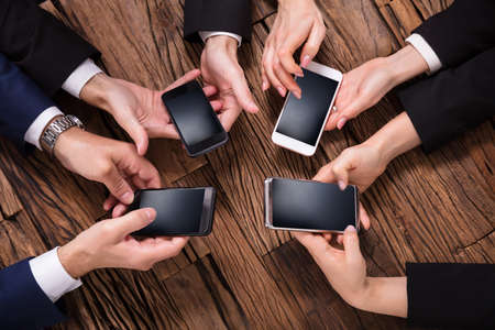 Elevated View Of Businesspeople Using Mobile Phone Over Wooden Deskの写真素材