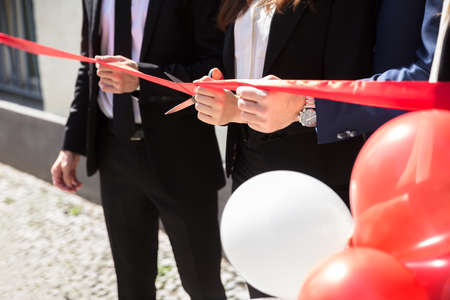 Close-up Of Businesspeople Hand Cutting Red Ribbon With Scissorsの写真素材