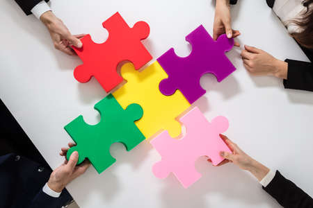 Group Of Businesspeople Solving Multi Colored Jigsaw Puzzle On Deskの写真素材