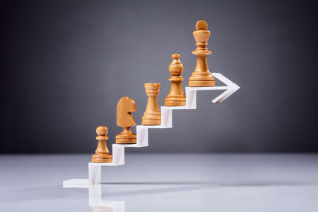 Wooden Chess Piece On Increasing Zigzag Arrow Against Grey Backdropの写真素材