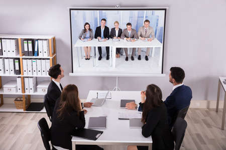Group Of Businesspeople Looking At Projector With Laptop On Desk In Officeの写真素材