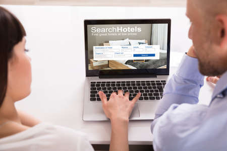Close-up Of Couple Searching Online Hotels On Laptop Over Deskの写真素材