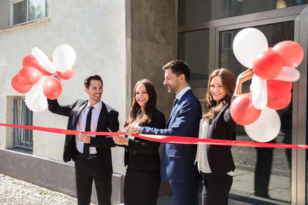 Portrait Of Smiling Young Businesspeople Cutting Red Ribbon