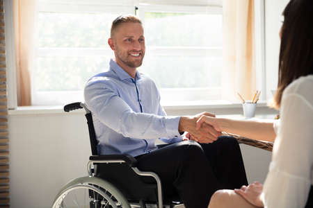 Happy Disabled Businessman Sitting On Wheelchair Shaking Hand With His Partnerの写真素材