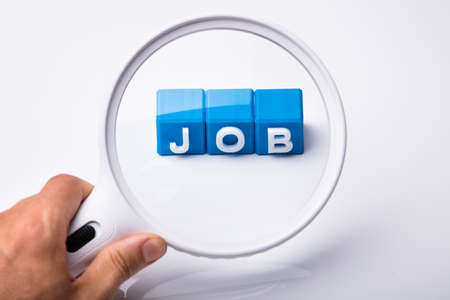 Close-up Of A Person's Hand Looking At Job Blocks Through Magnifying Glass On White Backgroundの写真素材