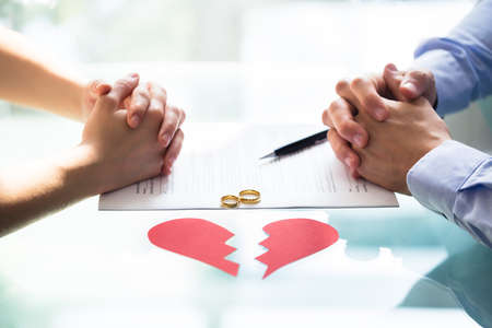 Couple's Hand On Divorce Paper With Wedding Rings And Broken Heartの写真素材
