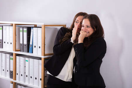 Young Businesswoman Whispering Into Female Colleague's Earの写真素材
