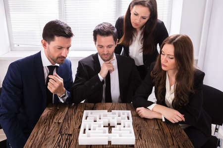 Group Of Young Businesspeople Trying To Solve Maze Puzzle At Workplace