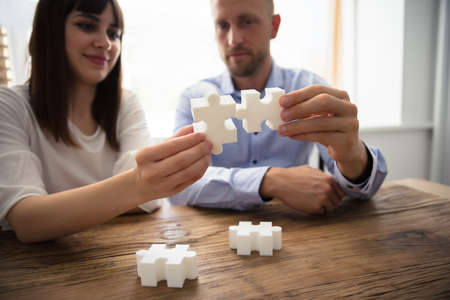 Close-up Of Two Businesspeople White Jigsaw Pieces Over Wooden Deskの写真素材